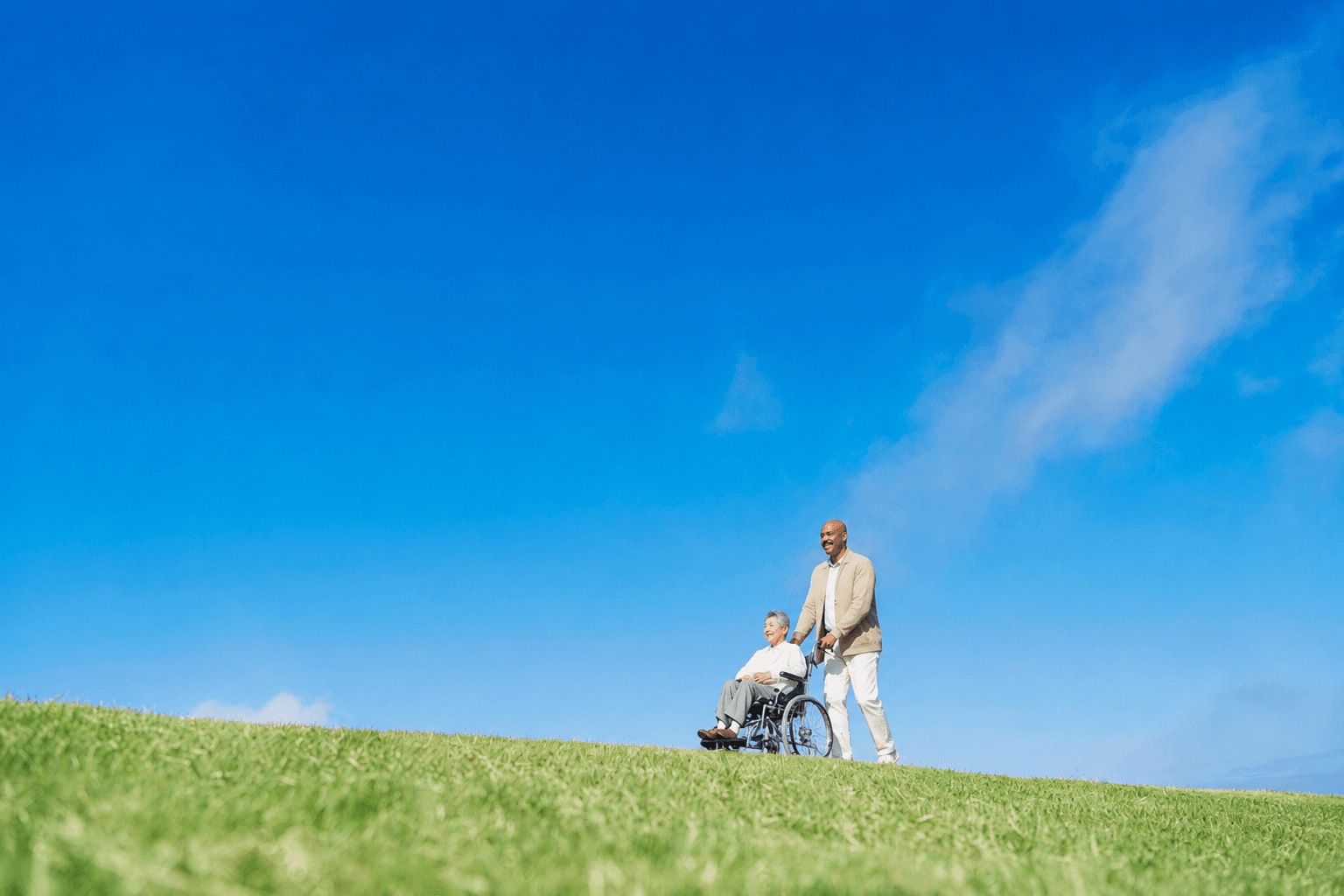 A caregiver assisting an older adult in a wheelchair outdoors